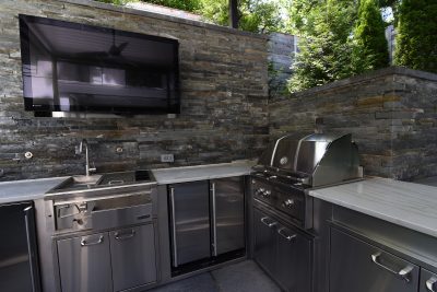 Outdoor kitchen with grill and sink, TV and hand chiseled stone wall